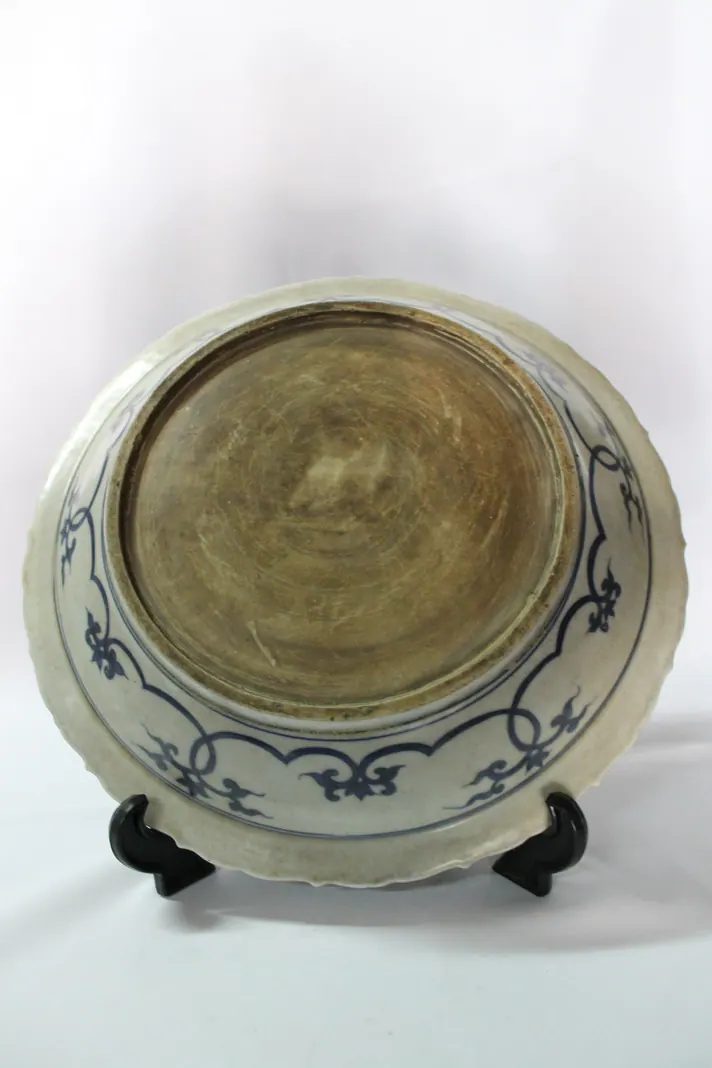 Base of a blue and white dish on a stand, showing the unglazed footring and a blue scroll border