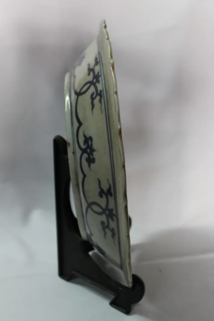 Side profile of a blue and white dish on a stand, showing the scroll border on the exterior