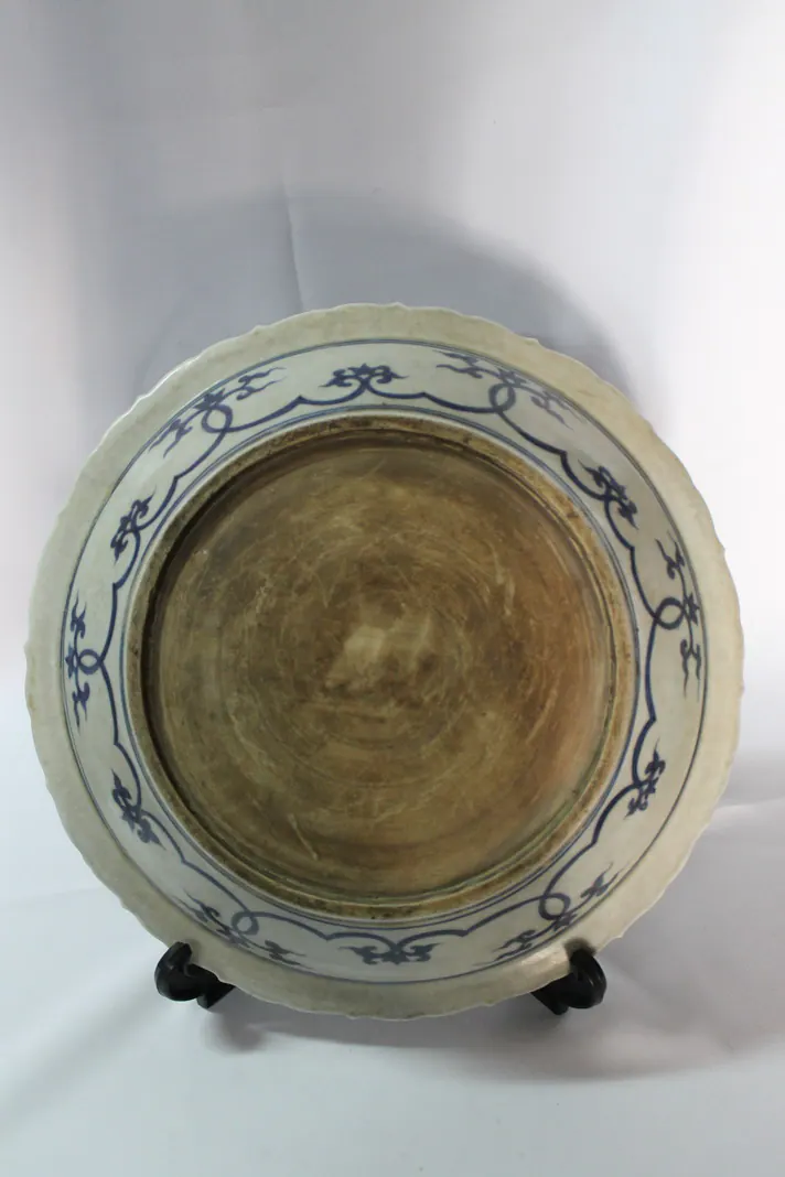 Base of a blue and white dish on a stand, showing the unglazed centre within a blue scroll border