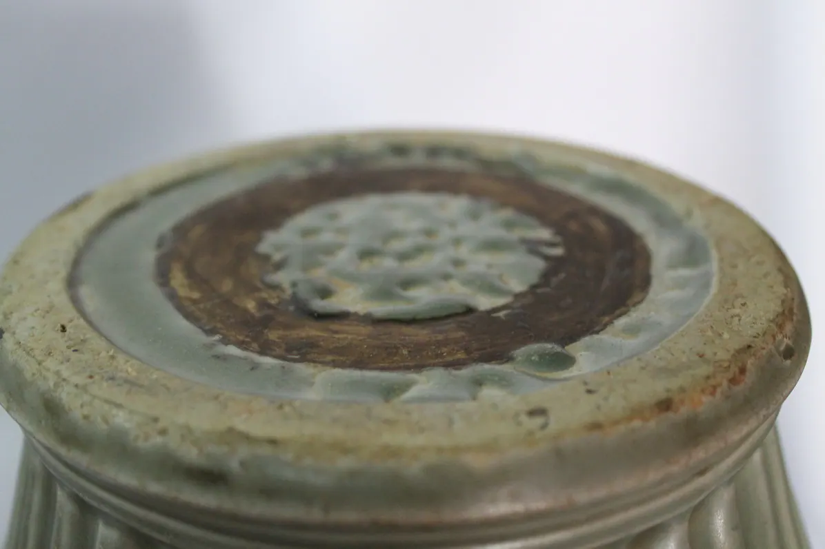 Close-up of the vase's foot showing rust-toned crackle spots in the celadon glaze