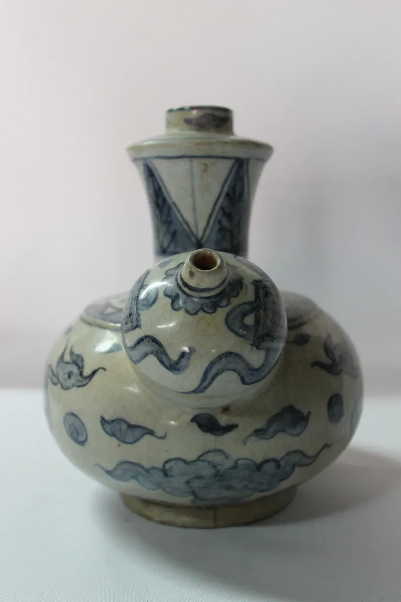 Blue and white kendi seen head-on, looking onto the spout, with clouds on the body