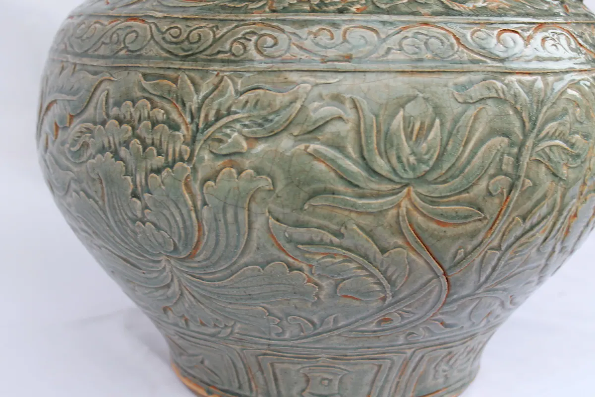 Detail of carved lotus and peony scrollwork on the jar's body, above a panel band near the foot