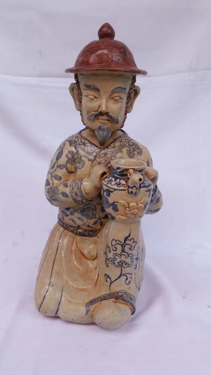 跪姿人像正面，头戴红色圆锥帽，手持青花小罐