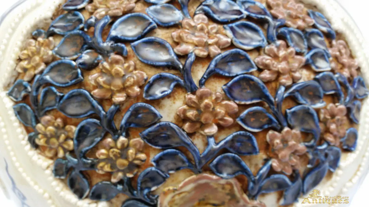 Close-up of the moulded floret medallion showing blue leaves and copper-brown flowers in high relief
