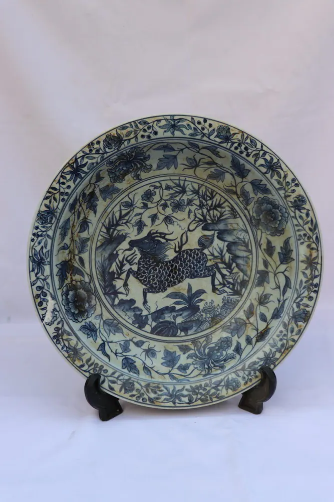 Front view of a blue and white porcelain plate with a Qilin in a landscape, double-ring medallion and floral rim