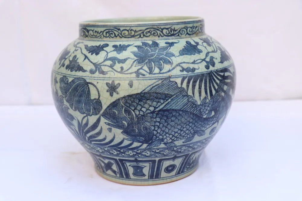 Front view of the jar showing a large scaled fish amid aquatic plants beneath a floral neck band