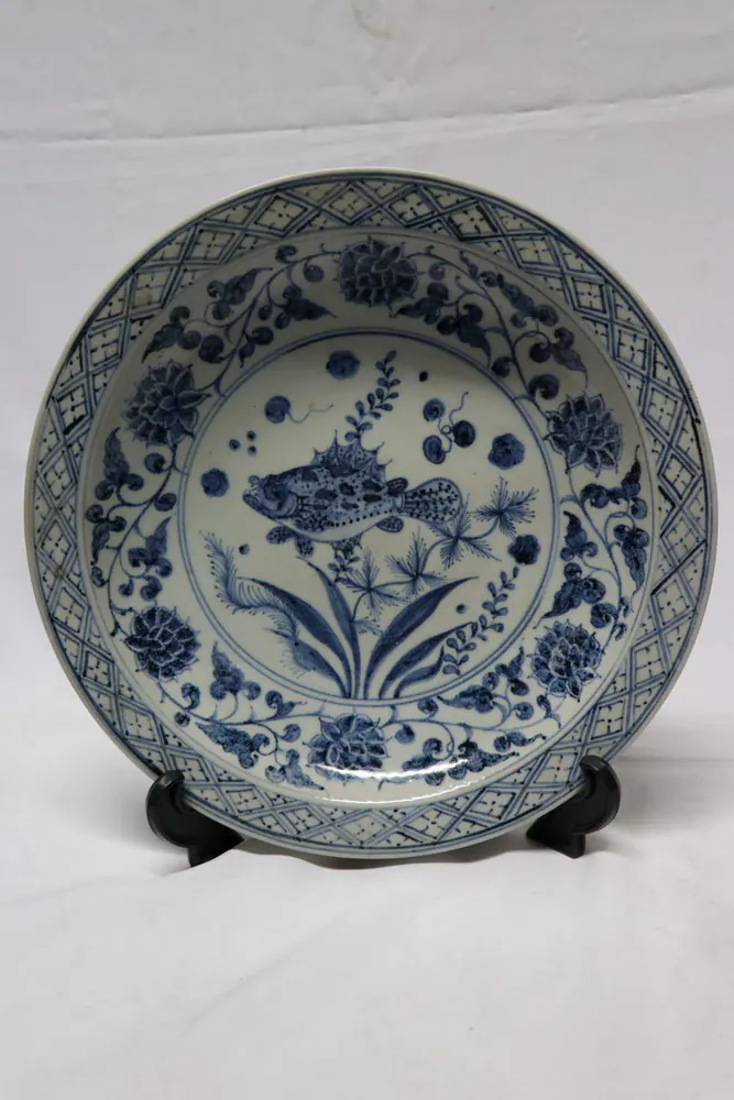 Front view of the plate on a stand, showing a fish among aquatic plants within a lattice-bordered rim