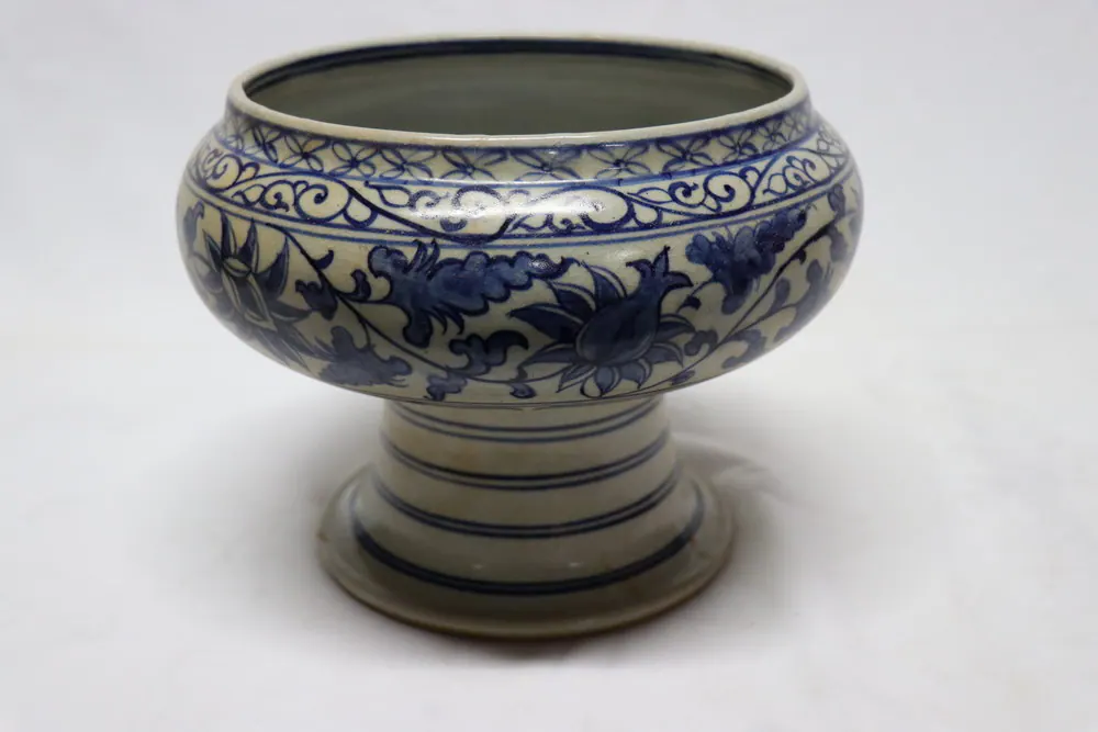 Blue and white stem cup with a floral scroll body, wave-pattern rim band and ribbed pedestal foot, front view