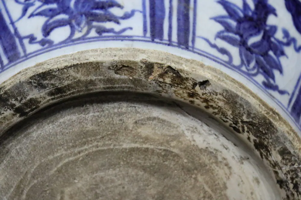 Close-up of the foot rim showing dark firing marks along the unglazed edge below a floral panel