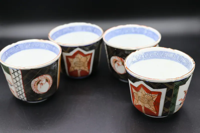 Four enamelled porcelain cups grouped together, each with a red star-shaped flower medallion on black lattice ground