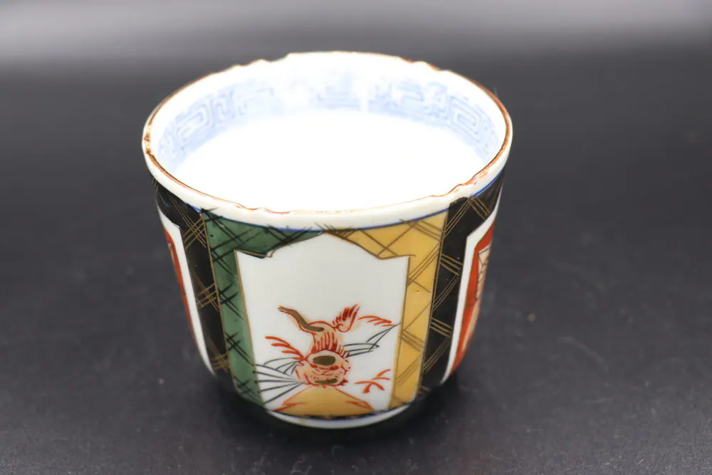 Front view of an enamelled cup showing a red bird motif within a white panel beside a diamond lattice ground