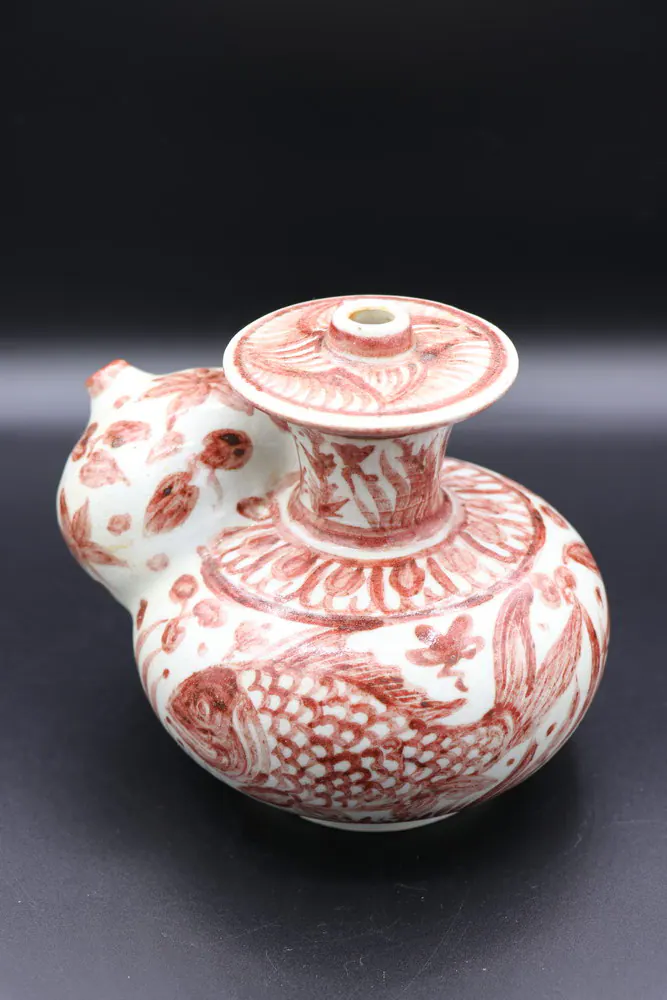 Front view of the kendi with a pierced domed spout, fish design, and a floral-banded neck