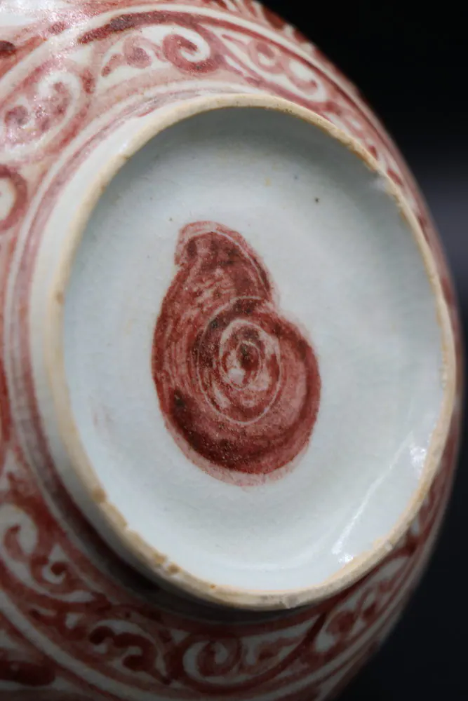 Close view of the kendi's base with the red spiral shell mark centred within a scroll border
