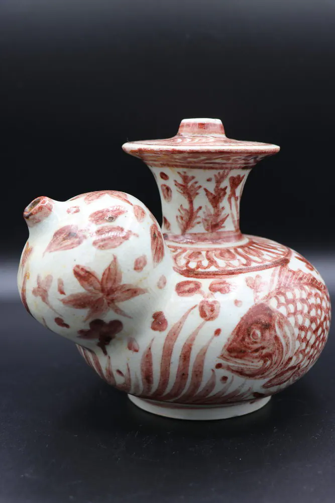 Side view of the kendi with the spout at left, floral neck, and fish design on the lower body