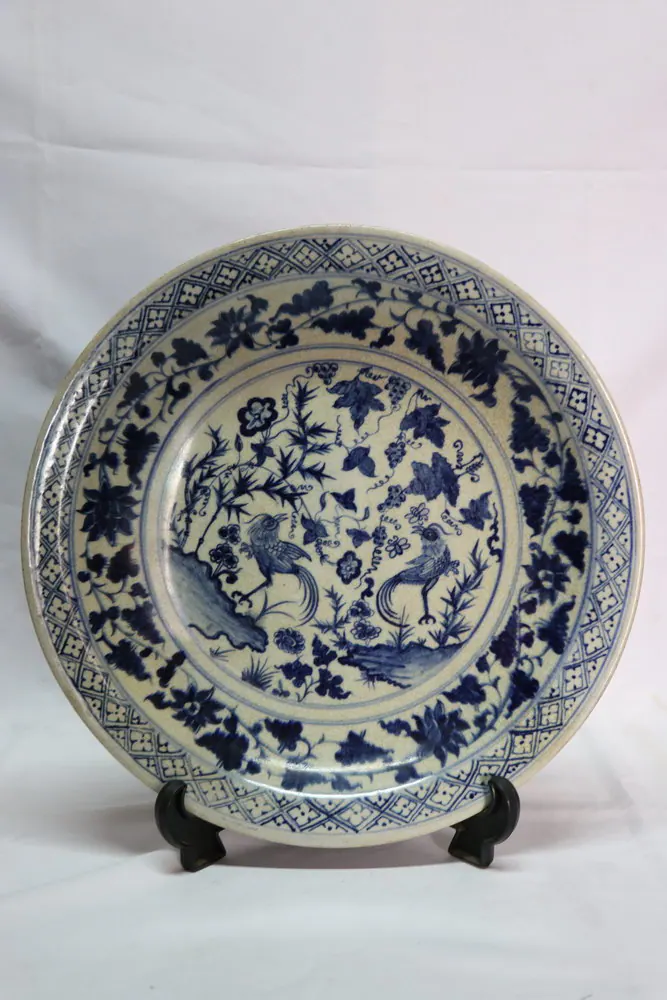 Front view of the blue and white charger plate with a floral scroll rim and a central medallion of birds among peonies