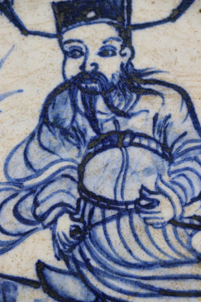 Close-up of the robed figure with a tall hat and beard, holding a round drum
