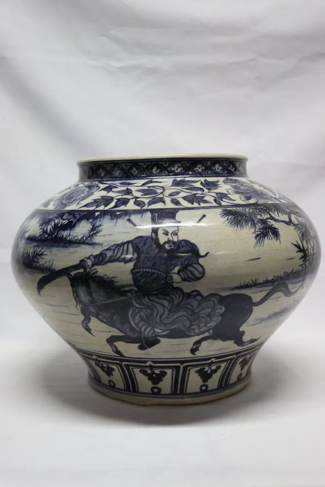 Squat blue and white jar with a mounted warrior wielding a sword within a wooded landscape