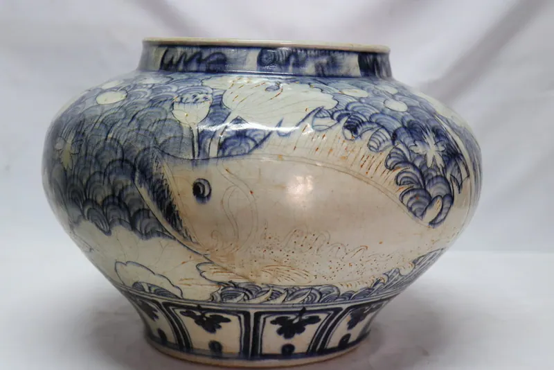 Front view of the jar showing a scaled fish motif on the shoulder above a wave band and lotus foot panels