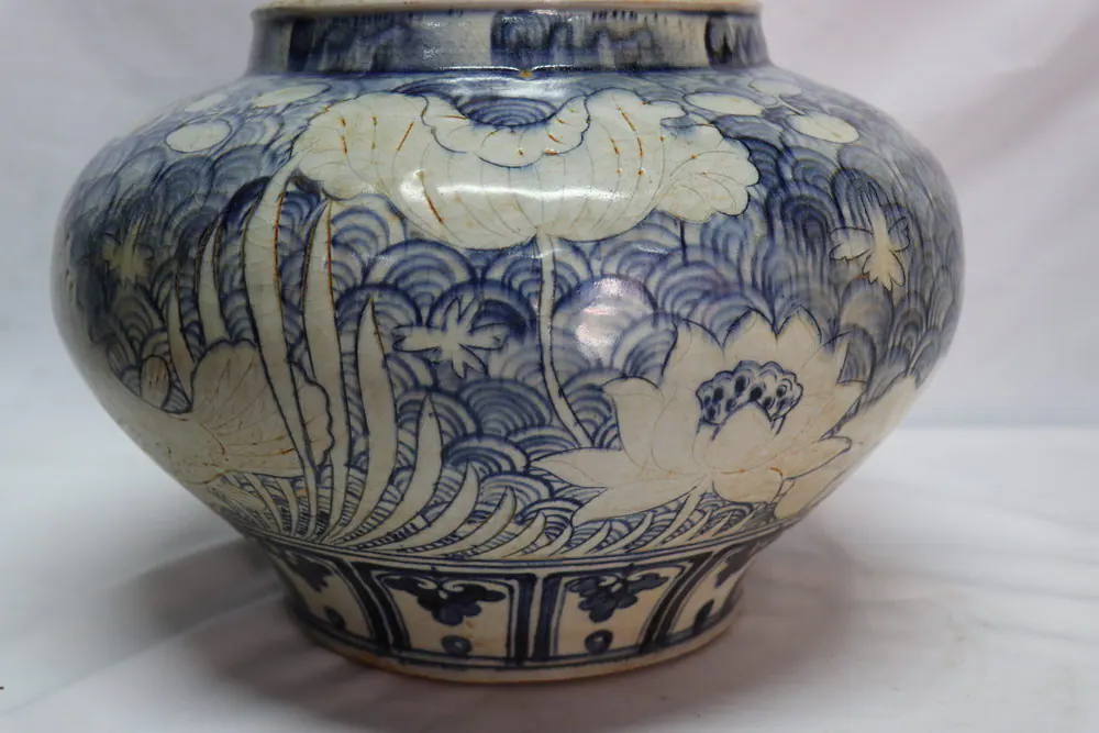 Blue and white jar viewed from an angle, showing reserved fish and lotus motifs against a wave-scale ground