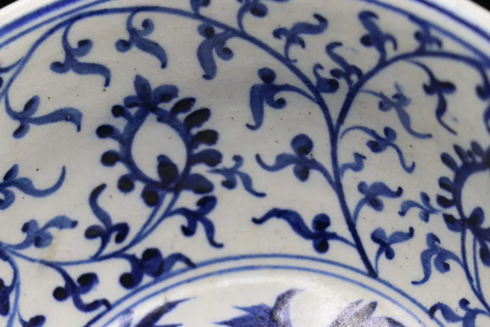 Close-up of a leafy scroll pattern with seed pods in underglaze blue on the bowl's surface