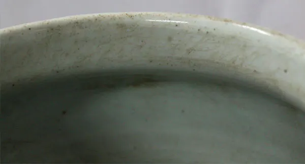 Close-up of a pale glazed porcelain rim and interior with fine surface scratches and dark specks