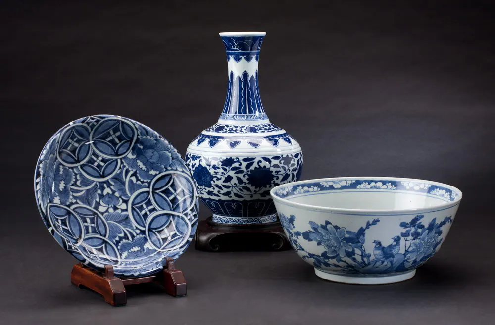 Blue and white dish, bottle vase and bowl displayed on wooden stands against a dark background