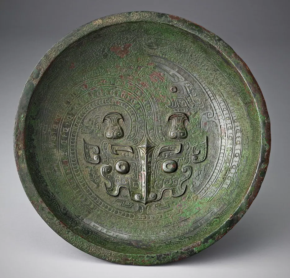 Bronze basin with green patina, its interior cast with a large mask face and scrolling bands
