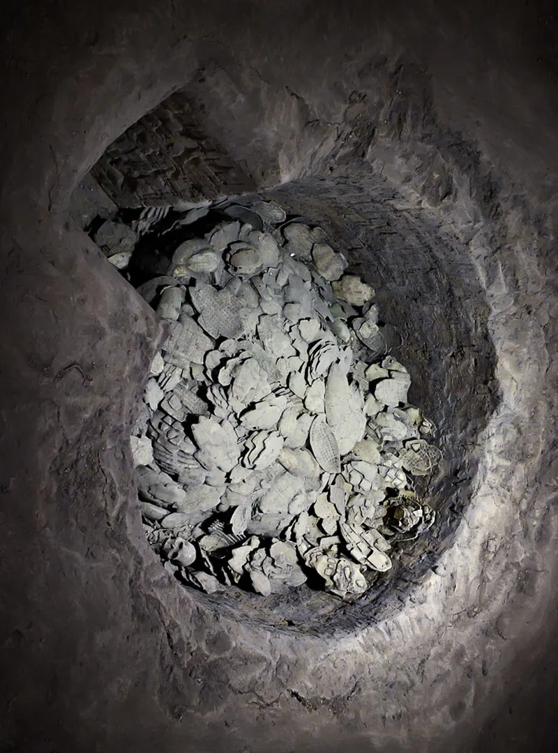 Overhead view of an excavated circular pit filled with heaped grey ceramic fragments