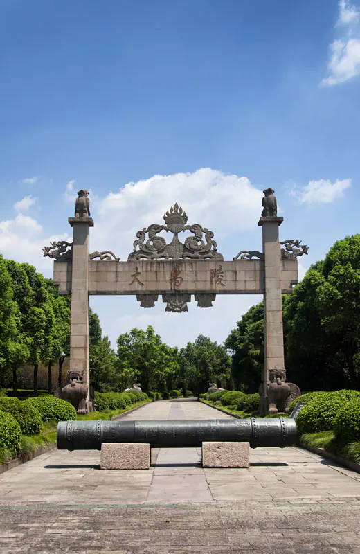 Stone memorial gateway inscribed 大禹陵, with carved dragons above and a long cannon on stone blocks before it