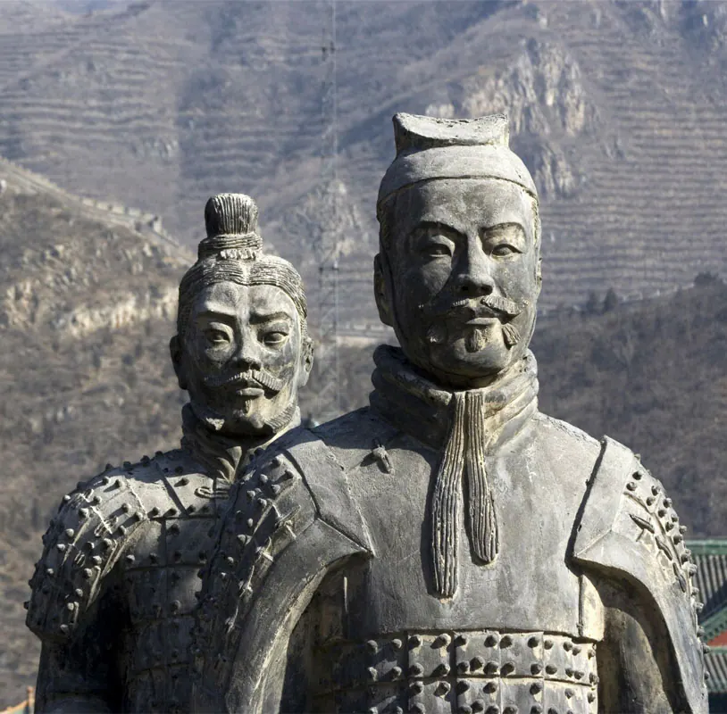两尊灰色石雕披甲武士像，背景为梯田般的山坡