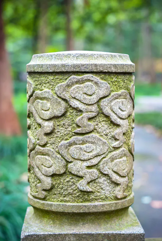 Moss-covered stone post carved with cloud scrolls, in a green garden
