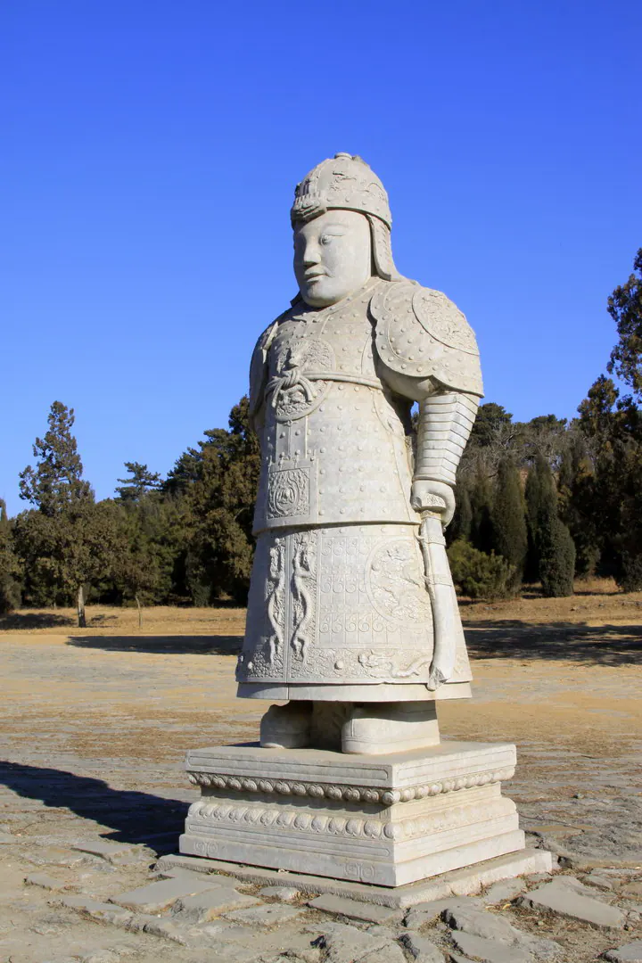 身披铠甲、手持剑的石雕武士像立于基座之上，背景为蓝天
