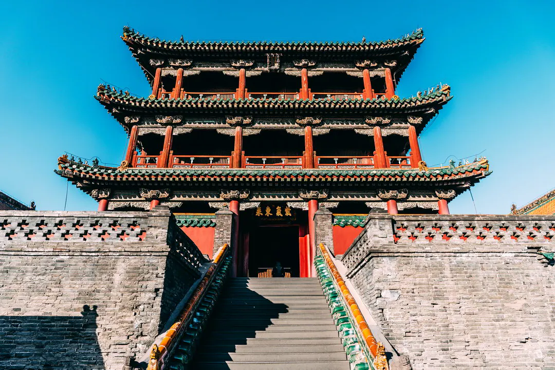 三层塔楼，有红柱与绿瓦檐，位于砖墙与中央阶梯之上
