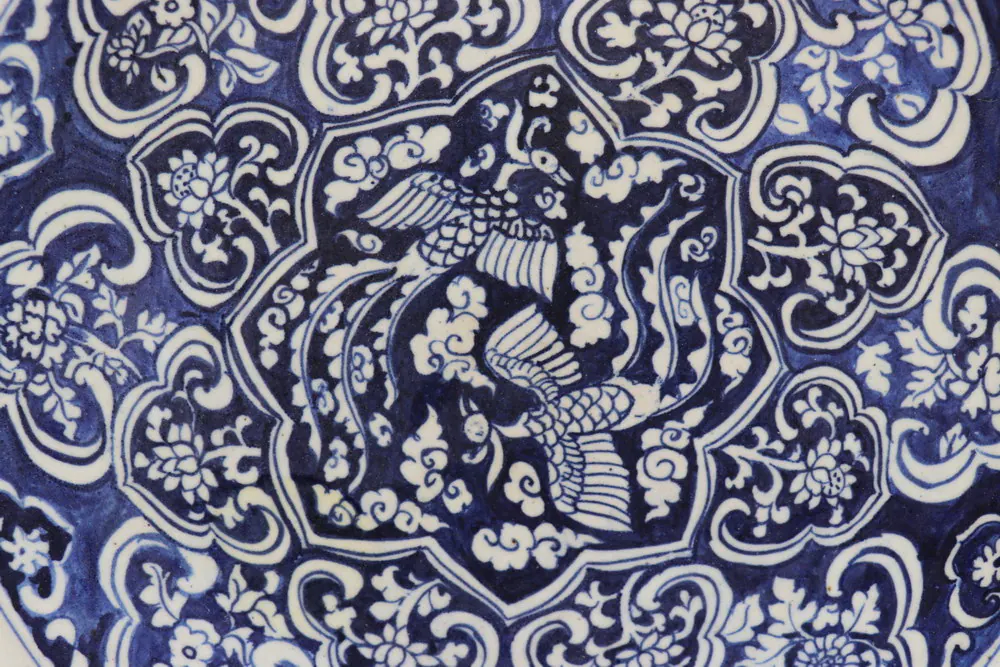 Close-up of a blue and white phoenix among clouds in a lobed panel, ringed by floral cartouches