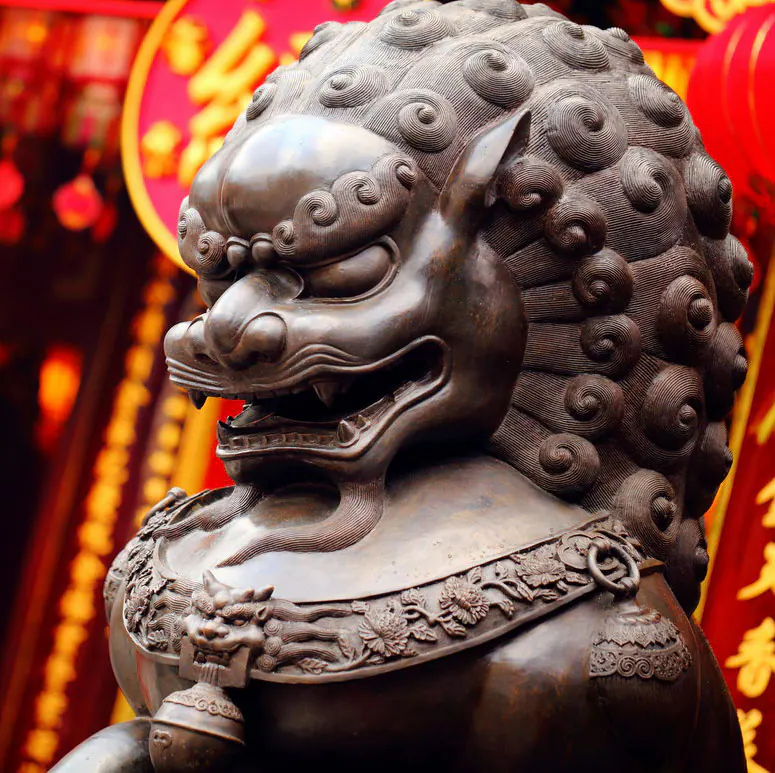 銅獅鬃毛捲曲，頸飾花環，立於紅色廟門前
