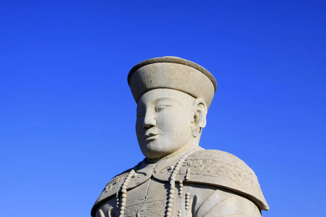 石雕官员像,头戴宽檐帽,佩朝珠,背景为深蓝天空