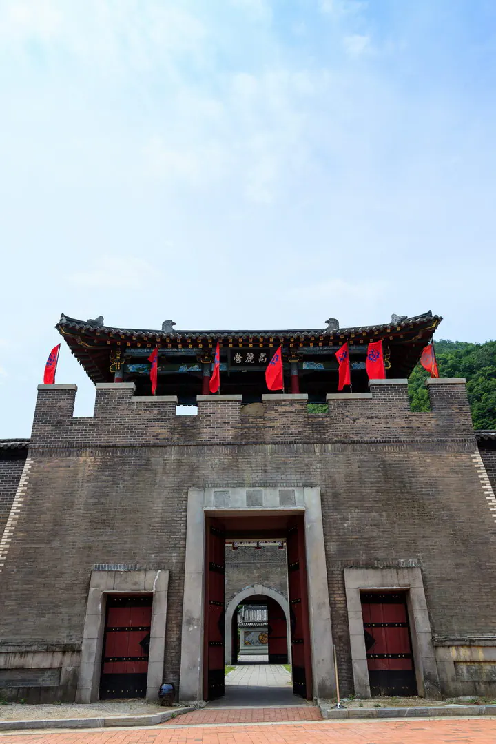 砖砌门楼配红门和红旗,顶上有带顶的楼阁,匾额题“高丽营”