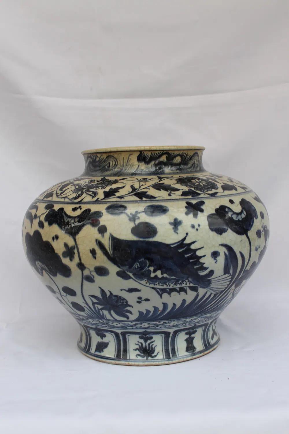 Side view of a large blue and white jar with a fish among lotus and water weeds