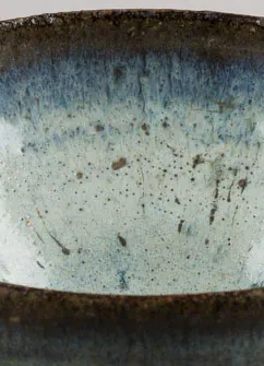 Close-up of a bowl interior with a milky pale blue glaze and brown flecks below a dark rim