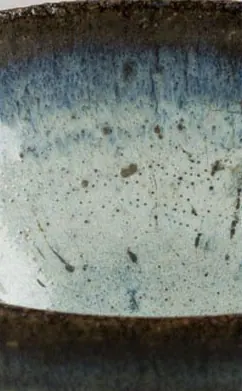 Close-up of a bowl interior with a milky pale blue glaze and brown flecks below a dark rim