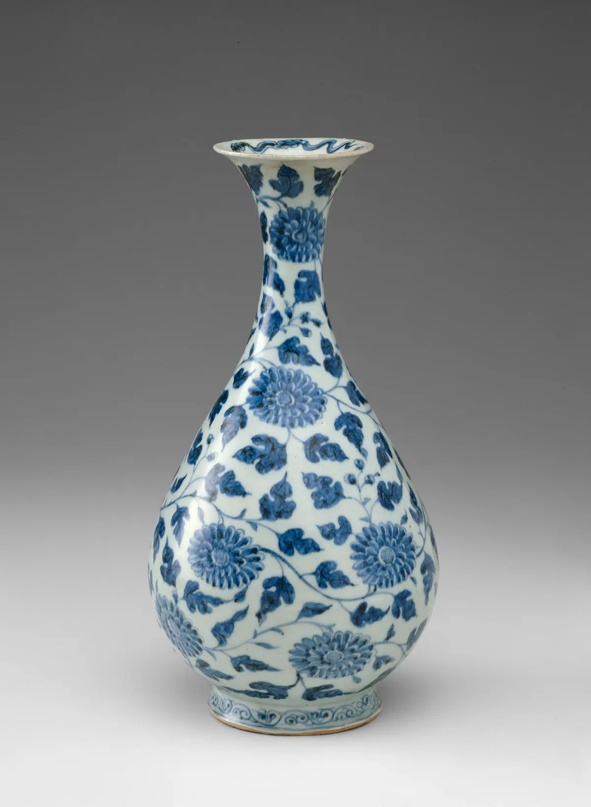 An early Ming blue and white pear-shaped bottle vase with a flared mouth, painted all over with large stylised flowers on a scrolling leafy stem, with a small scroll band at the foot.