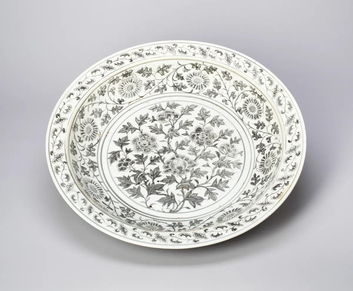 A large early Ming dish painted in underglaze copper red that has fired grey-black, with a peony spray in the centre, a chrysanthemum scroll around the well and a small floral scroll on the rim.