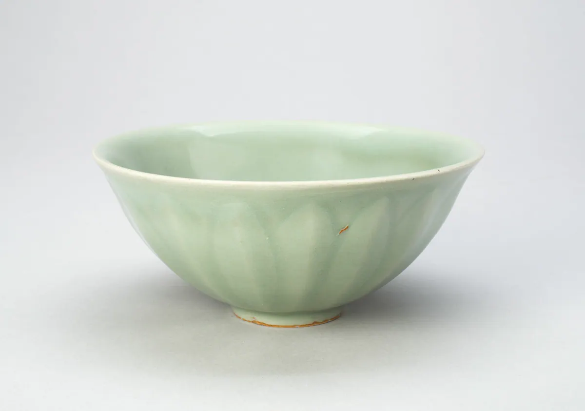 A Longquan celadon bowl with flared sides and a small foot, carved outside with overlapping lotus petals under an even, soft sea-green glaze.