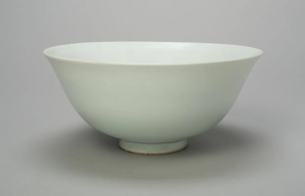 A deep white porcelain bowl with flared sides and a small foot, under an opaque, slightly bluish egg-white glaze, seen from the side so that the decoration inside is out of view.