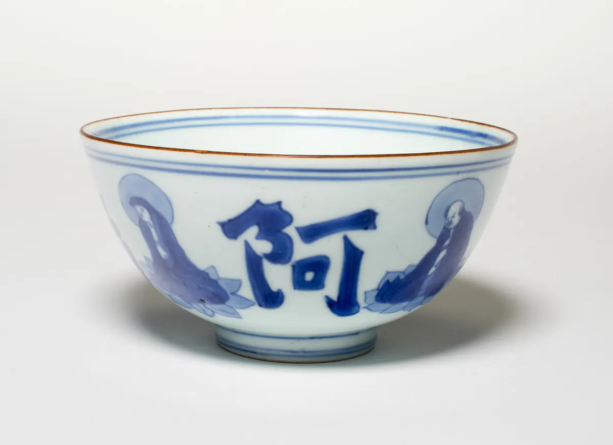 A blue and white bowl with a brown-edged rim, painted with haloed luohans seated on lotus pads between large calligraphic characters, with double blue lines at the rim and foot.