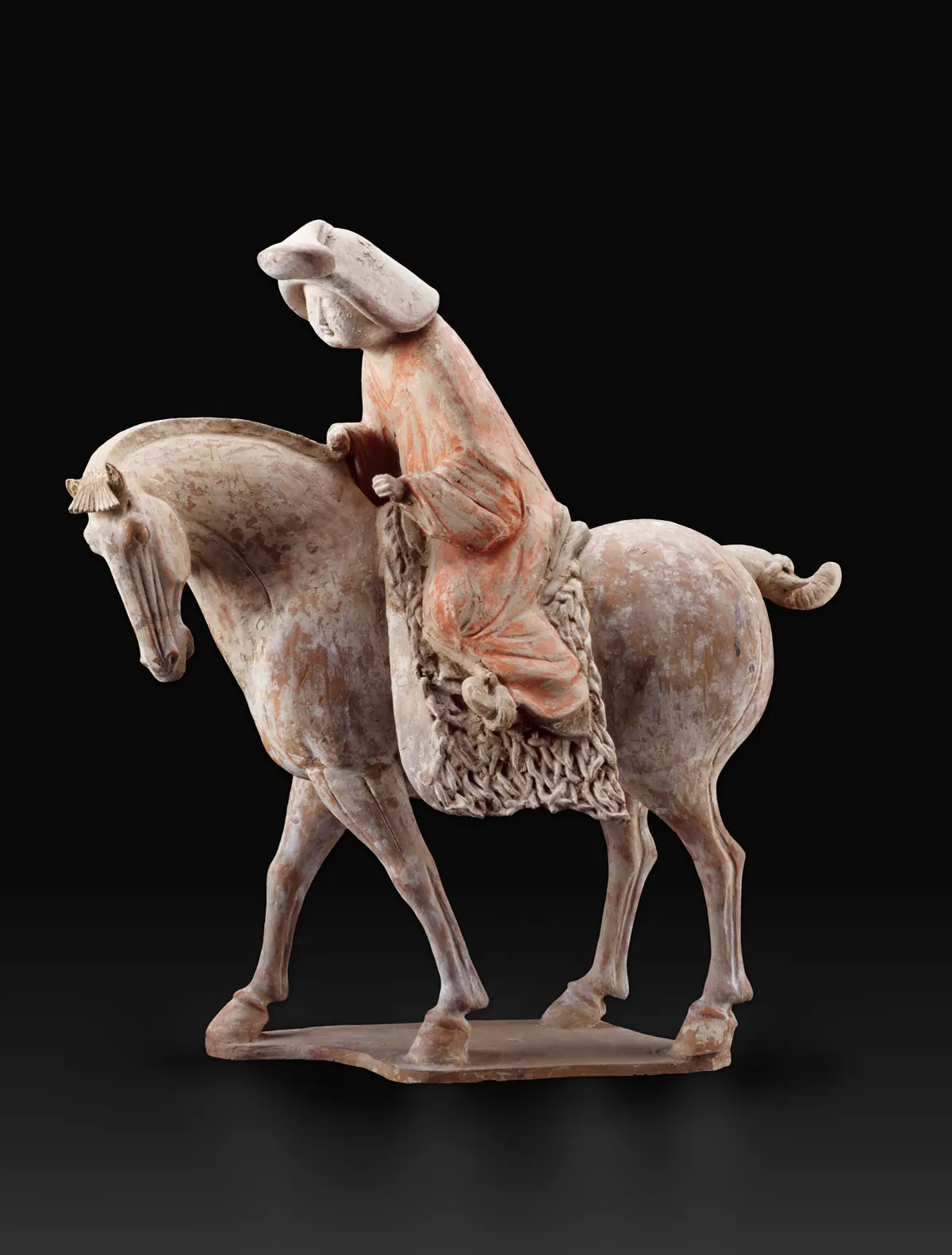 Painted earthenware tomb figure of a woman riding a walking horse, wearing a broad hat and a long red-painted robe, seated on a fringed saddle cloth.