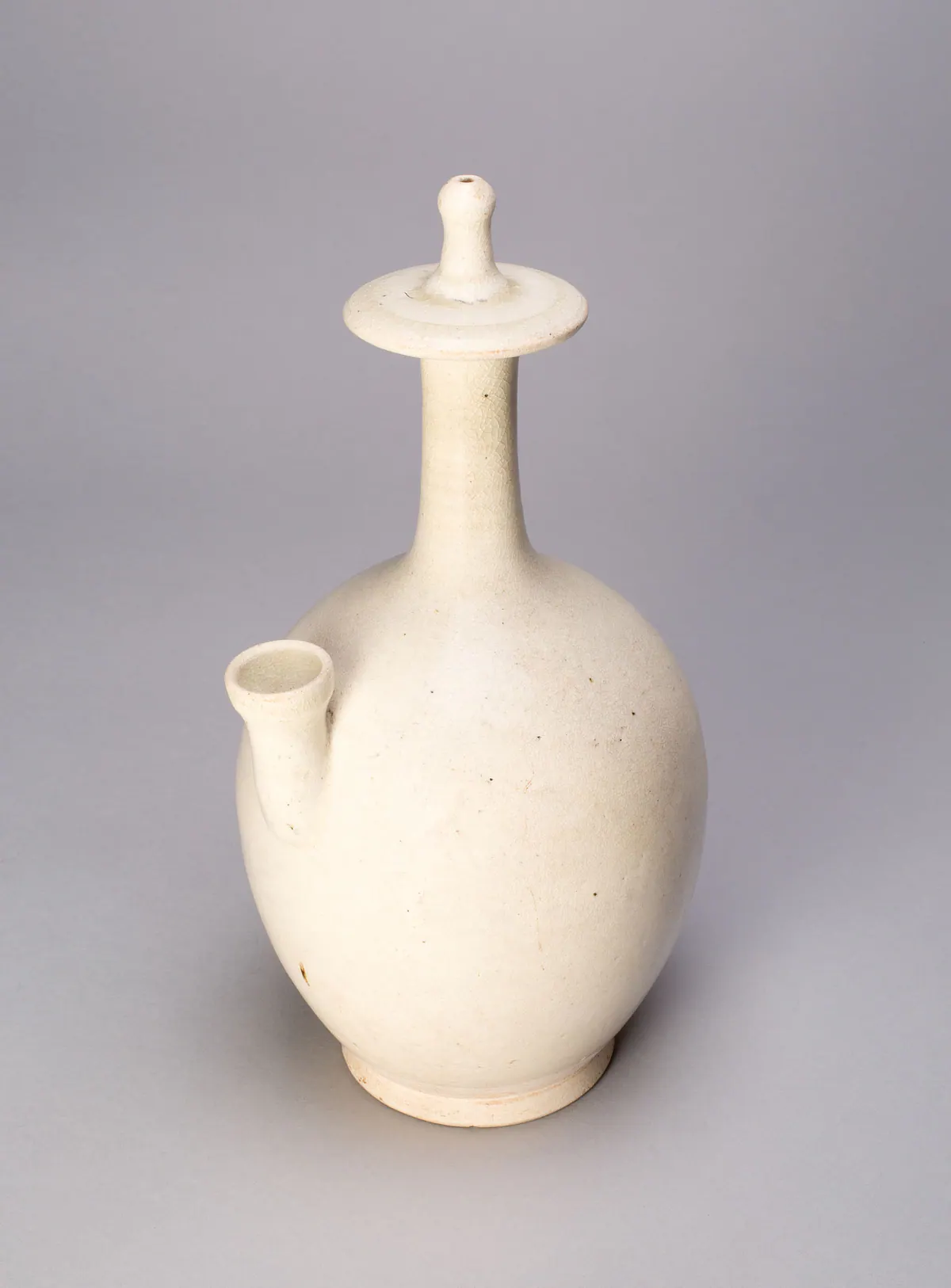 A northern white ware kundika, or Buddhist water sprinkler, with an ovoid body, a short side spout and a tall slender neck with a flat disc, under a finely crackled creamy white glaze.