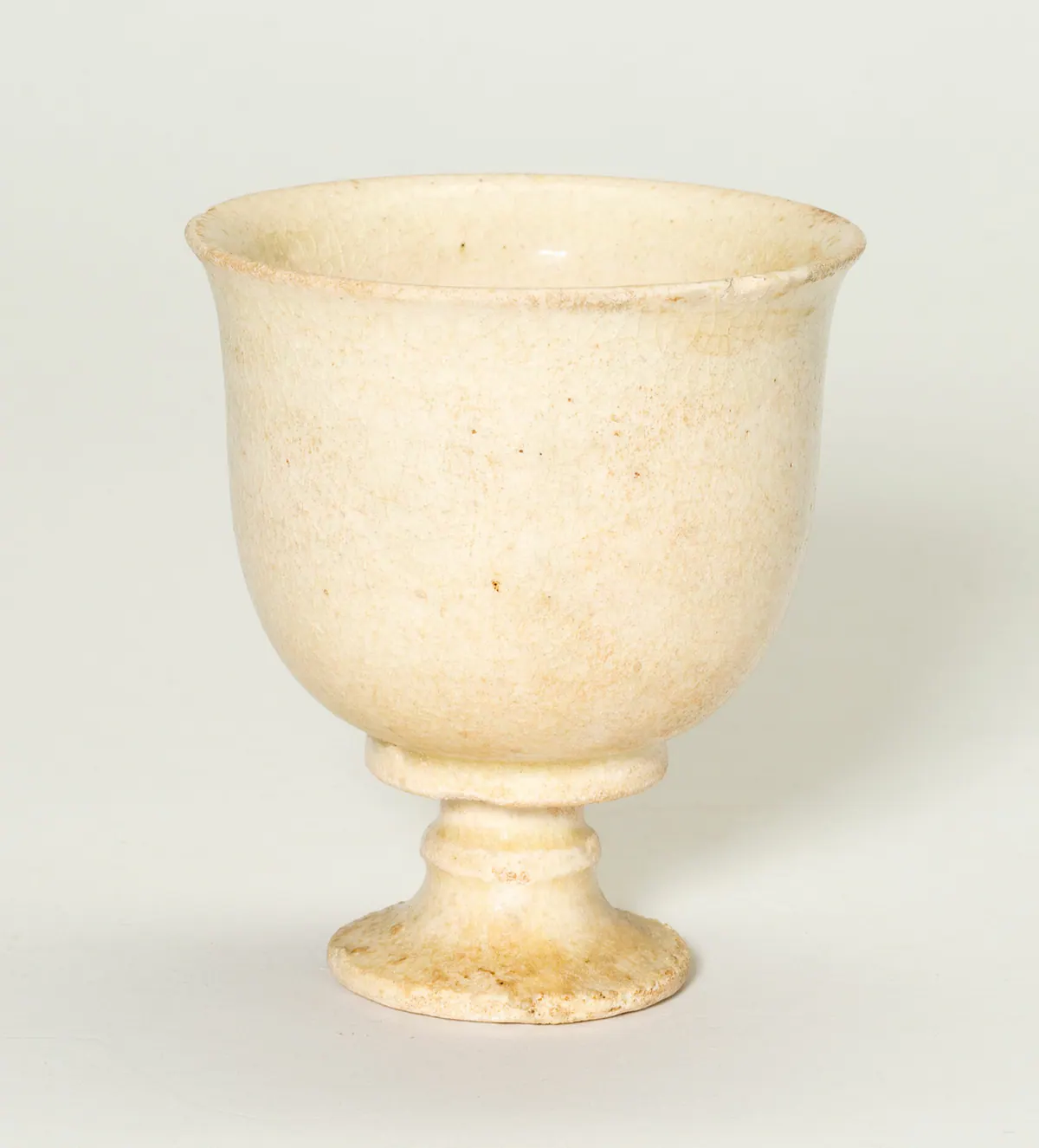 A small stoneware stem cup with a deep rounded bowl, a ringed stem and a spreading foot, covered in a finely crackled ivory-white glaze.