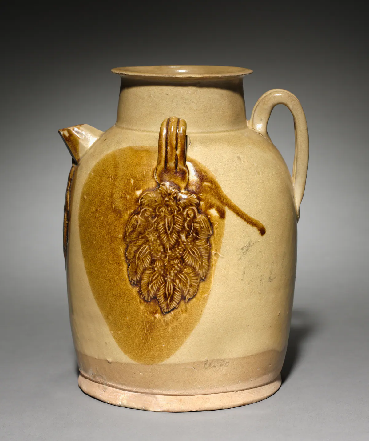 A Changsha ware stoneware ewer with a short spout and strap handle, its straw-coloured glaze decorated with a moulded floral appliqué set in a large brown glaze patch.