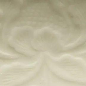 Close-up inside a Ding bowl, about 3 cm across: a warm ivory glaze over a moulded peony, its petals and dotted centre picked out by light and shadow